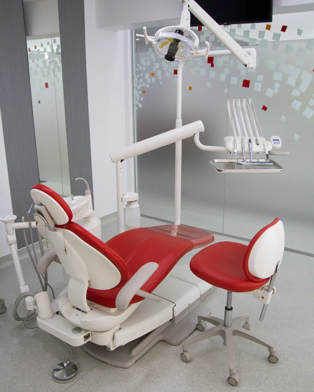 A treatment room at our partner clinic in Bucharest, with a red dental chair, overhead light and instrument tray ready for a patient